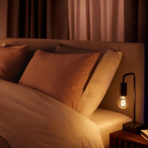 Lâmpada inteligente Philips Hue White Ambiance 7W 2200-4500K Fil 550lm A60 E27 em uma luminária de mesa