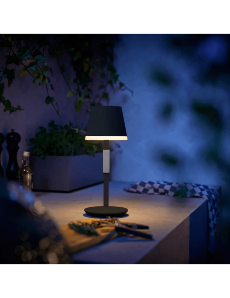 Lámpara de mesa portátil LED inteligente Hue Go negro-gris encendida en una mesa