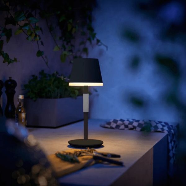 Lámpara de mesa portátil LED inteligente Hue Go negro-gris encendida en una mesa